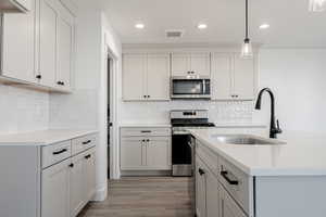 Kitchen with sink, hanging light fixtures, stainless steel appliances, tasteful backsplash, and light hardwood / wood-style floors