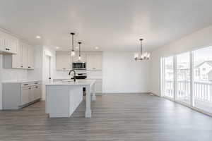 Kitchen featuring a center island with sink, sink, appliances with stainless steel finishes, decorative light fixtures, and white cabinetry