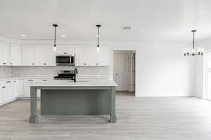 Kitchen featuring stainless steel appliances, sink, decorative light fixtures, white cabinetry, and an island with sink