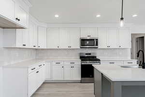 Kitchen featuring pendant lighting, sink, appliances with stainless steel finishes, light stone counters, and white cabinetry