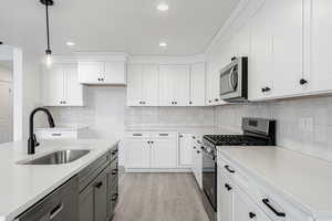 Kitchen with sink, decorative light fixtures, light stone counters, white cabinetry, and stainless steel appliances