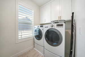 Clothes washing area with washing machine and dryer, cabinets, and light wood-type flooring