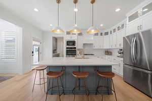 Kitchen with backsplash, decorative light fixtures, a center island with sink, appliances with stainless steel finishes, and light wood-type flooring