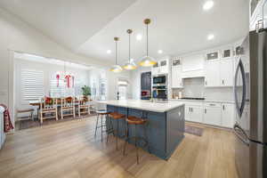 Kitchen featuring appliances with stainless steel finishes, a kitchen island with sink, decorative light fixtures, light hardwood / wood-style floors, and white cabinetry