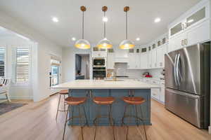 Kitchen featuring a center island with sink, light wood-type flooring, stainless steel appliances, and hanging light fixtures