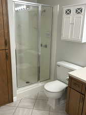 Features a shower with shower door, vanity, tile flooring, and toilet