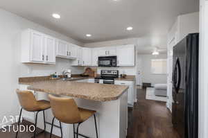 Kitchen featuring black appliances, dark hardwood / wood-style flooring, sink, a breakfast bar, and kitchen peninsula