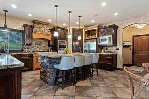 Kitchen featuring decorative backsplash, appliances with stainless steel finishes, premium range hood, and a kitchen island with sink