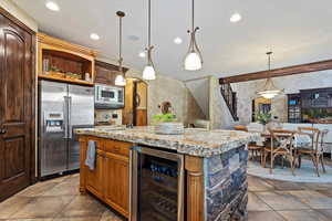 Kitchen featuring beverage cooler, an island with sink, tile patterned floors, hanging light fixtures, and appliances with stainless steel finishes