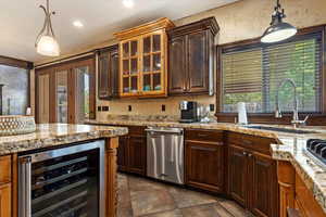 Kitchen with stainless steel dishwasher, decorative light fixtures, sink, wine cooler, and dark tile patterned flooring