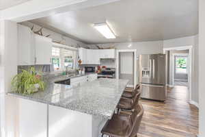 Kitchen featuring black appliances, white cabinets, sink, and light stone counters