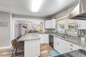 Kitchen featuring a breakfast bar, sink, dishwasher,  and wall chimney exhaust hood