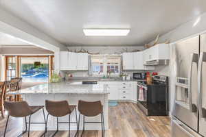 Kitchen featuring white cabinets, light stone counters, appliances with stainless steel finishes, and a kitchen breakfast bar