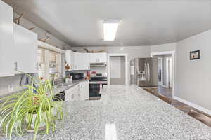 Kitchen featuring white cabinetry, stainless steel appliances, sink, and light stone countertops