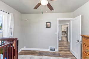 Bedroom featuring dark hardwood / wood-style floors, a crib, and ceiling fan