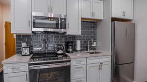 Kitchen featuring sink, appliances with stainless steel finishes, white cabinets, and backsplash