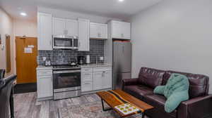 Kitchen featuring hardwood / wood-style flooring, stainless steel appliances, tasteful backsplash, and white cabinets