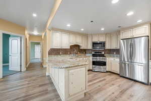 Kitchen featuring sink, cream cabinetry, light hardwood / wood-style floors, light stone counters, and stainless steel appliances