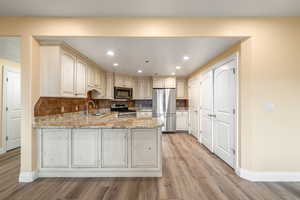 Kitchen featuring sink, light stone counters, backsplash, kitchen peninsula, and appliances with stainless steel finishes