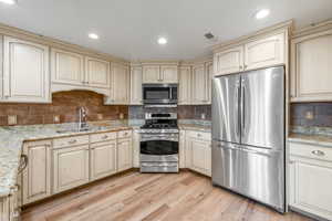 Kitchen featuring light wood-type flooring, light stone counters, stainless steel appliances, sink, and cream cabinets