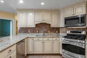 Kitchen featuring backsplash, light stone counters, stainless steel appliances, sink, and cream cabinets