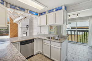 Kitchen with white cabinetry, wooden walls, light tile patterned floors, stainless steel dishwasher, and light stone countertops