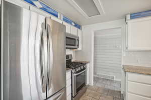 Kitchen featuring light tile patterned flooring, white cabinetry, decorative backsplash, and stainless steel appliances