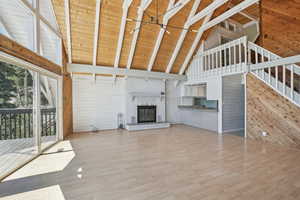 Unfurnished living room featuring beam ceiling, a brick fireplace, hardwood / wood-style floors, wooden ceiling, and high vaulted ceiling