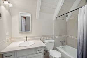 Full bathroom featuring vaulted ceiling with beams, vanity, shower / bath combo with shower curtain, and toilet