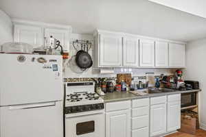 Kitchen with sink, white cabinetry, tasteful backsplash, and white appliances