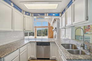 Kitchen with dishwasher, tasteful backsplash, and white cabinetry