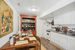 Kitchen featuring white cabinetry, a textured ceiling, white range with gas stovetop, decorative backsplash, and sink