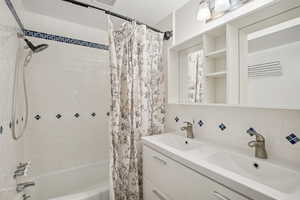 Bathroom featuring dual vanity, tasteful backsplash, shower / bath combo, and tile walls