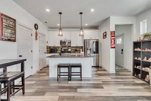 Kitchen featuring backsplash, hanging light fixtures, hardwood / wood-style floors, appliances with stainless steel finishes, and a center island with sink