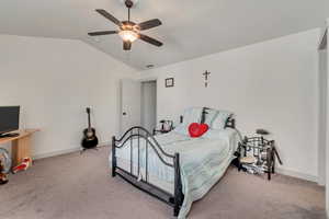 Carpeted bedroom featuring ceiling fan and vaulted ceiling