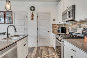 Kitchen with stainless steel appliances, sink, decorative light fixtures, white cabinetry, and wood-type flooring