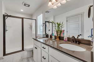 Bathroom with dual vanity, toilet, a shower with shower door, and tile patterned flooring