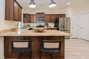 Kitchen featuring decorative light fixtures, a kitchen bar, appliances with stainless steel finishes, light hardwood / wood-style flooring, and kitchen peninsula