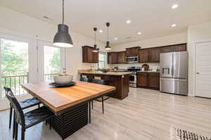 Kitchen featuring dark brown cabinetry, hanging light fixtures, stainless steel appliances, and a wealth of natural light