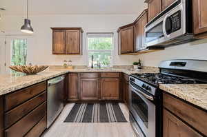 Kitchen featuring sink, light stone countertops, pendant lighting, and stainless steel appliances