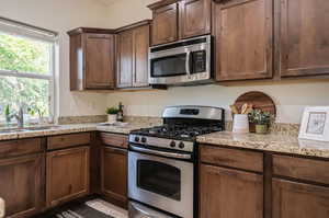 Kitchen featuring dark brown cabinets, light stone counters, appliances with stainless steel finishes, and sink