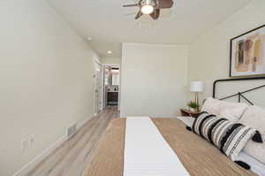 Bedroom featuring ensuite bathroom, ceiling fan, and light wood-type flooring