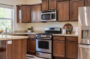 Kitchen featuring appliances with stainless steel finishes, light stone counters, and sink