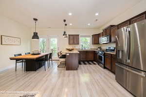 Kitchen featuring decorative light fixtures, light stone counters, appliances with stainless steel finishes, and light wood-type flooring