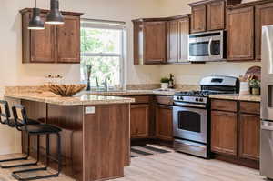 Kitchen featuring stainless steel appliances, pendant lighting, light wood-type flooring, light stone counters, and a breakfast bar