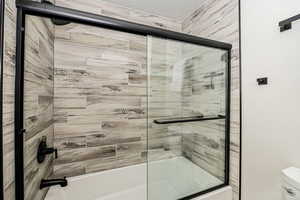 Bathroom with shower / bath combination with glass door and toilet