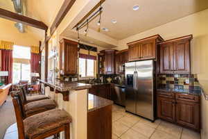 Kitchen featuring light tile patterned floors, vaulted ceiling with beams, stainless steel appliances, decorative backsplash, and kitchen peninsula