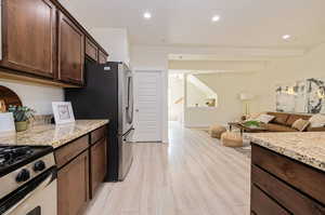 Kitchen with beam ceiling, light stone counters, dark brown cabinetry, stainless steel fridge, and light hardwood / wood-style flooring