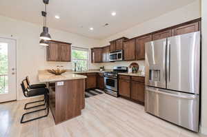 Kitchen featuring a breakfast bar area, stainless steel appliances, light stone countertops, decorative light fixtures, and dark brown cabinetry