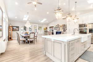 Kitchen featuring ceiling fan, an island with sink, light hardwood / wood-style floors, appliances with stainless steel finishes, and vaulted ceiling with skylight